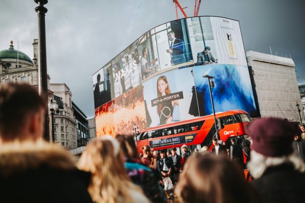 Crowd in front of large city LED billboards.