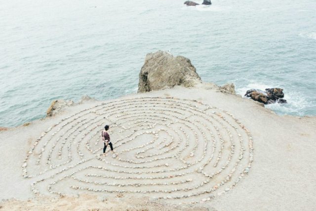 Person walking through a rock labyrinth by the ocean.