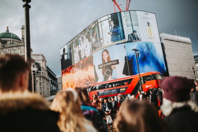 Crowd in front of large city LED billboards.