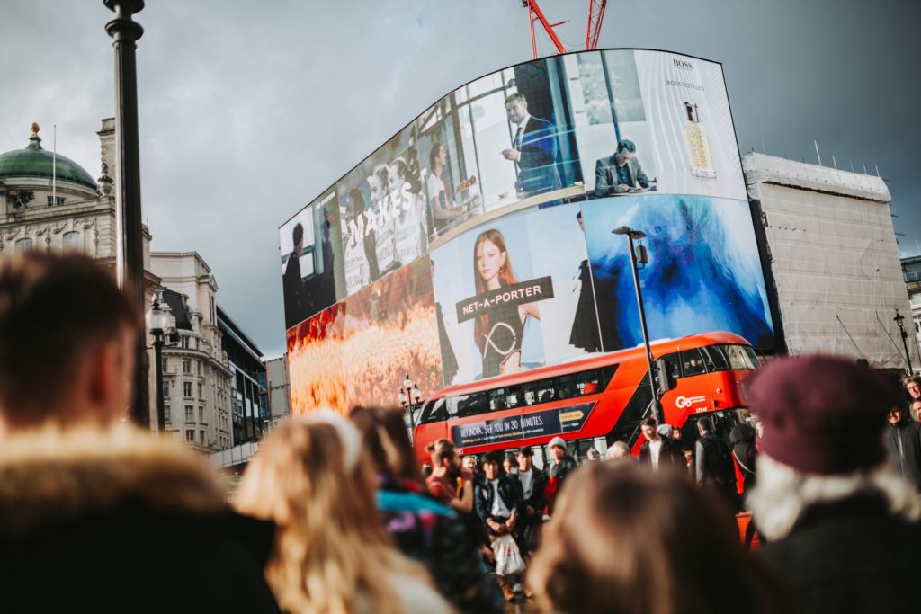 Crowd in front of large city LED billboards.