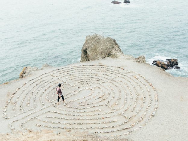Person walking in circular rock maze by the ocean.