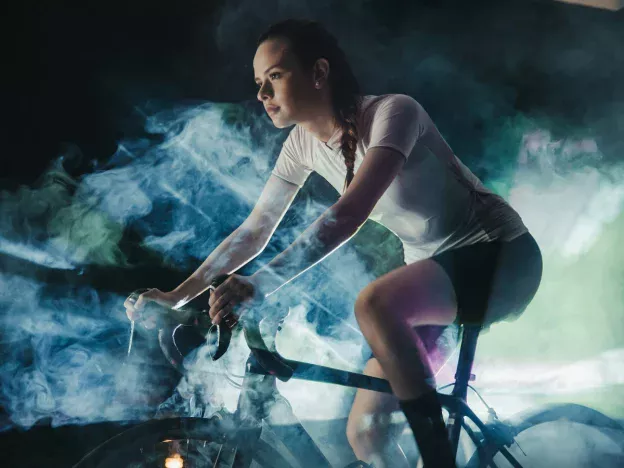 Woman cycling through colorful smoke indoors.