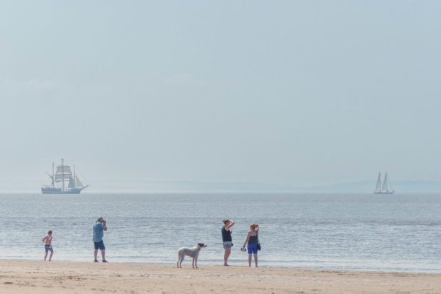 People on beach watching sailing ships in ocean