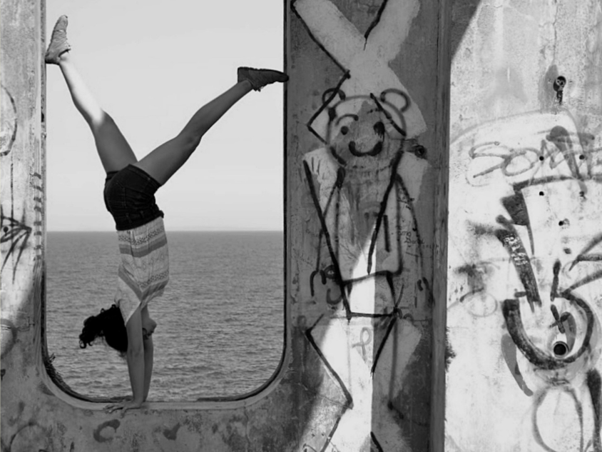 1 Person doing handstand in graffiti-framed window by ocean.